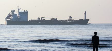 Another Place statue located on the Irish sea coast and floating tanker in Liverpool, United Kingdom